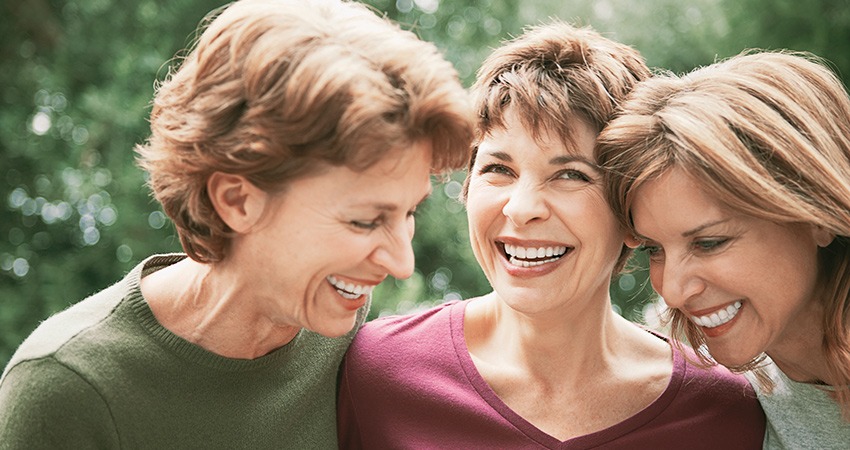 Three female friends laugh as they share their transformations with dental implants