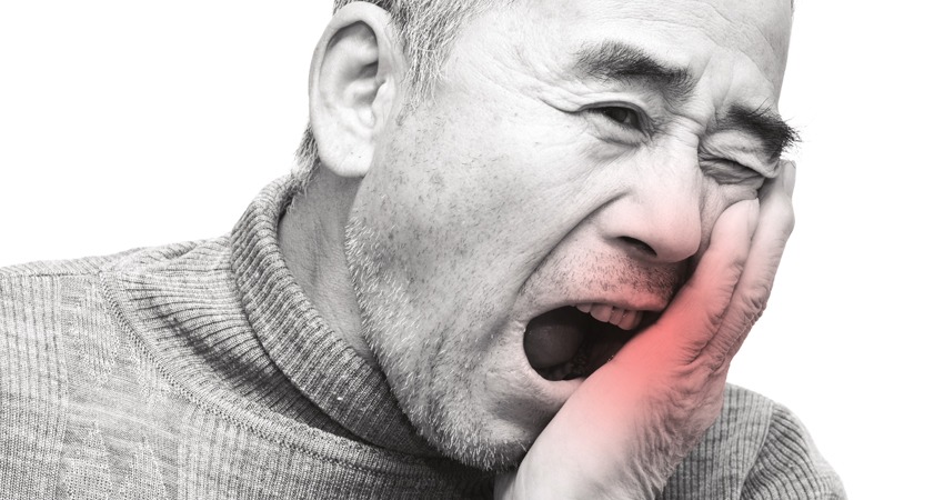 Man in need of a root canal treatment puts hand on face due to pain