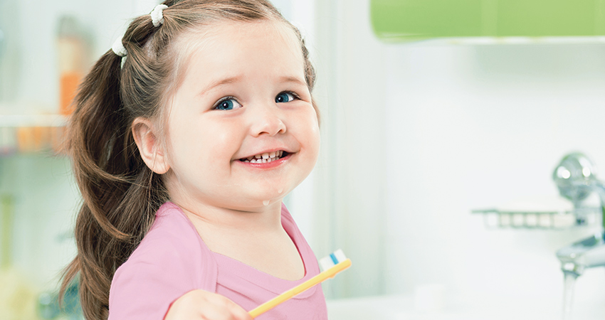 a happy toddler girl smiling and holding a toothbrush
