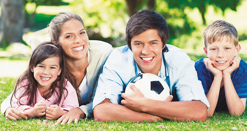 Family lies on grass and shows off their smiles that underwent Invisalign treatment